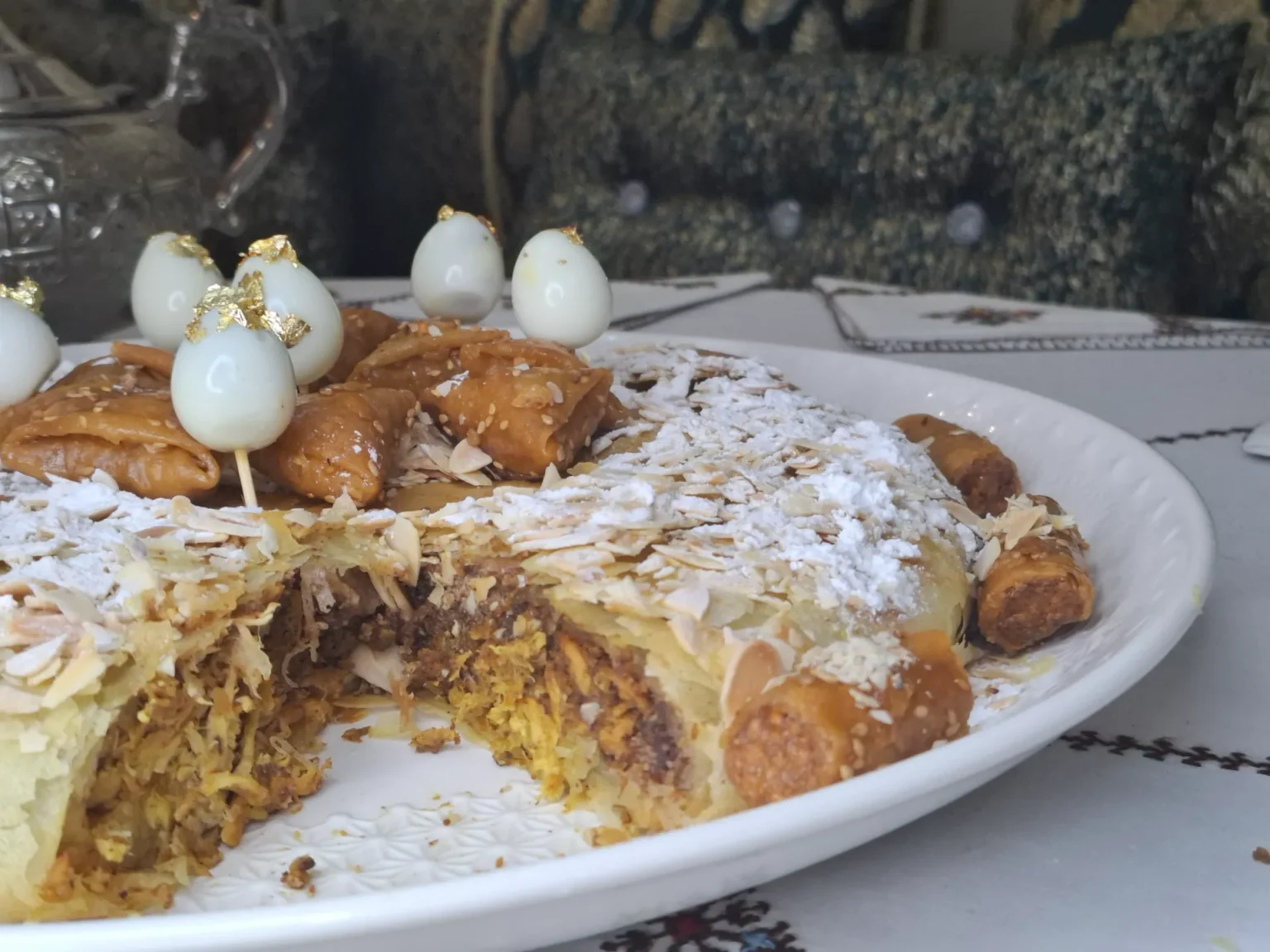 Pastilla marocaine au poulet et amandes, richement décorée avec œufs de caille sur piques dorées, sucre glace, cannelle, et accompagnée de petites pâtisseries au miel.